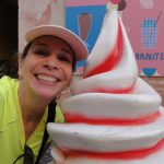 lady in a green shirt and pink hat, next to a giant plastic ice cream swirl