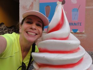 lady in a green shirt and pink hat, next to a giant plastic ice cream swirl