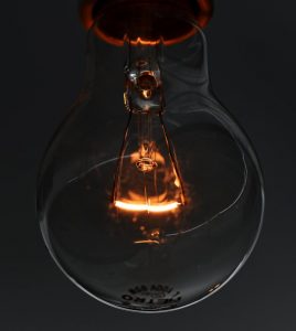 clear lightbulb against black background with a gold filament shining