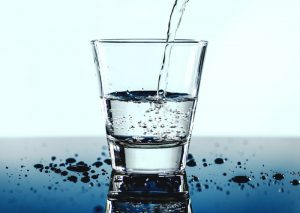drinking glass being filled with water, with water drops on the blue tabletop
