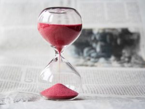 hourglass with red sand pouring from the top half to the bottom, displayed on top of a newspaper
